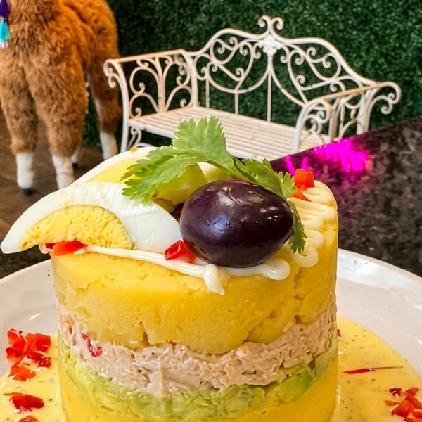 Layered Peruvian causa rellena with egg, olive, and cilantro, in a restaurant with a llama decoration.