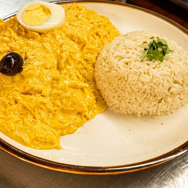Aji de Gallina with white rice, a hard-boiled egg, and a black olive on a plate.