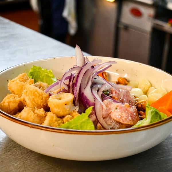 A bowl of ceviche with fried calamari, red onions, corn, and sweet potato on a kitchen counter.
