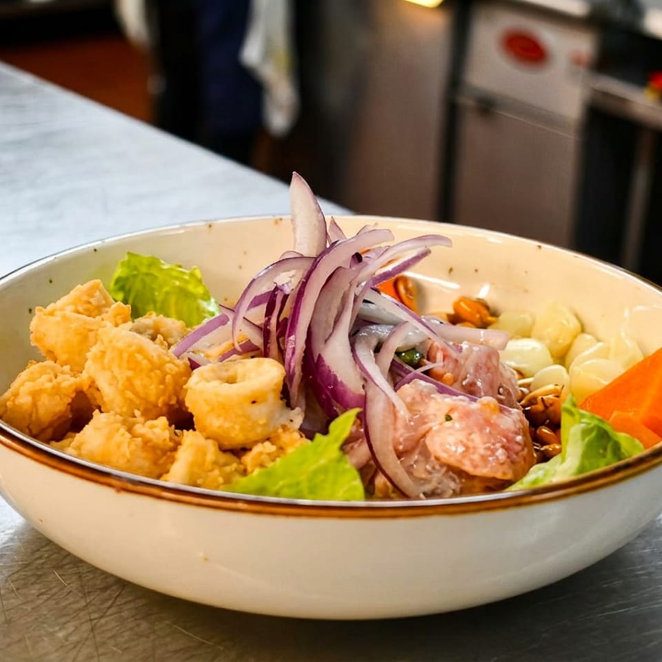 Bowl of ceviche with fried calamari, red onions, corn, and sweet potato on a metal counter.